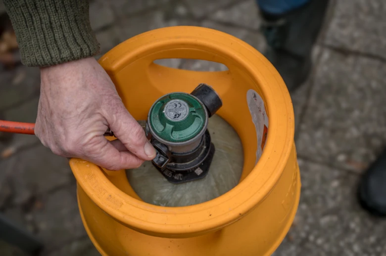 Ruka otvírá ventil na malé žluté plynové lahvi v nosiči.