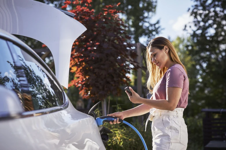 Žena nabíjí elektromobil venku pomocí modrého kabelu.