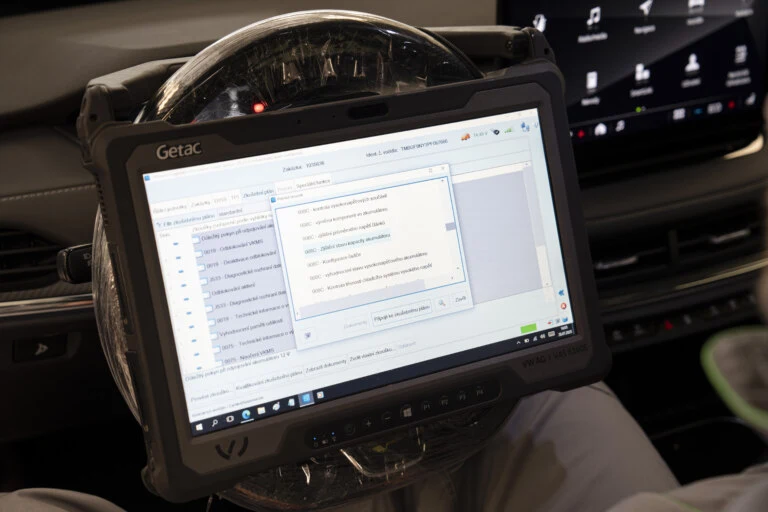 Tablet s diagnostickým programem pro kontrolu baterie elektromobilu v autě.