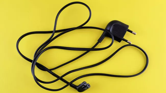 Černý elektrický prodlužovací kabel s dvěma zástrčkami na žlutém pozadí.