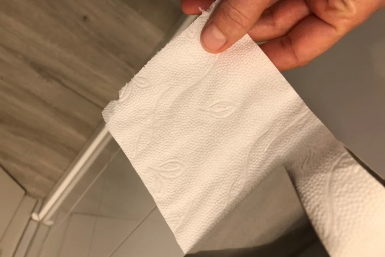 Ruka drží kus toaletního papíru v koupelně.