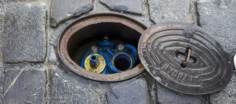Otevřený kryt požárního hydrantu na dlažbě s viditelnými ventily.