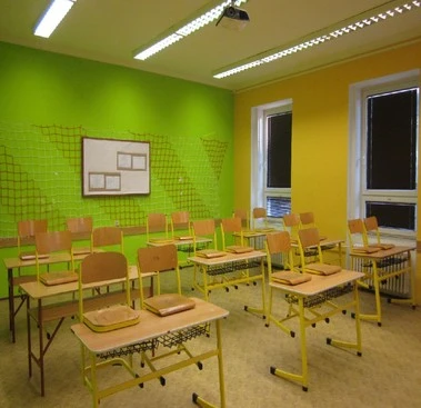 Školní třída s okny pro přirozené světlo a stropními lampami pro umělé osvětlení.