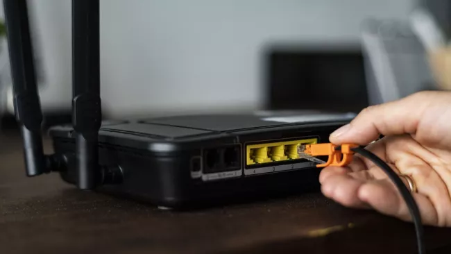 Ruka připojuje ethernetový kabel k modemu pro síťové rozšíření.