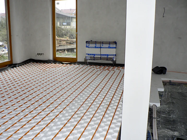 Instalace podlahového vytápění s oranžovými hadicemi na bílém izolantu.