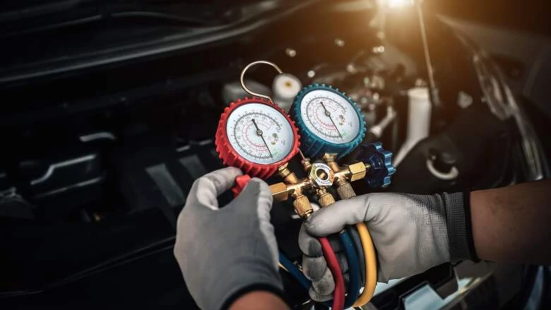 Technik používá manometr pro plnění klimatizace freonem pod kapotou auta.