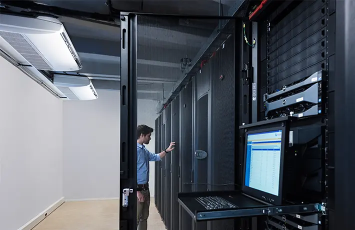 Technik v serverovně s klimatizačními jednotkami nad řadami servery.