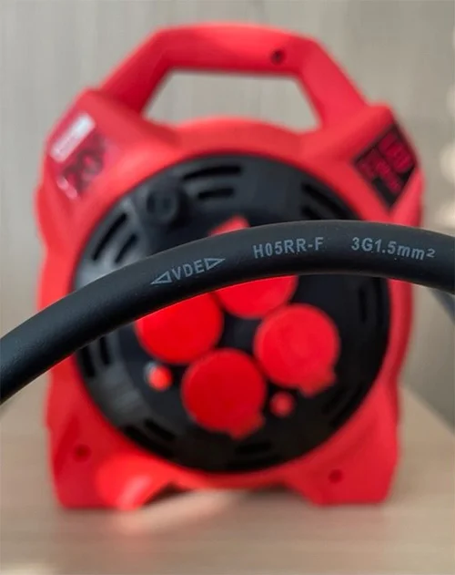 Černý prodlužovací kabel s technickými údaji před červenou zásuvkou.