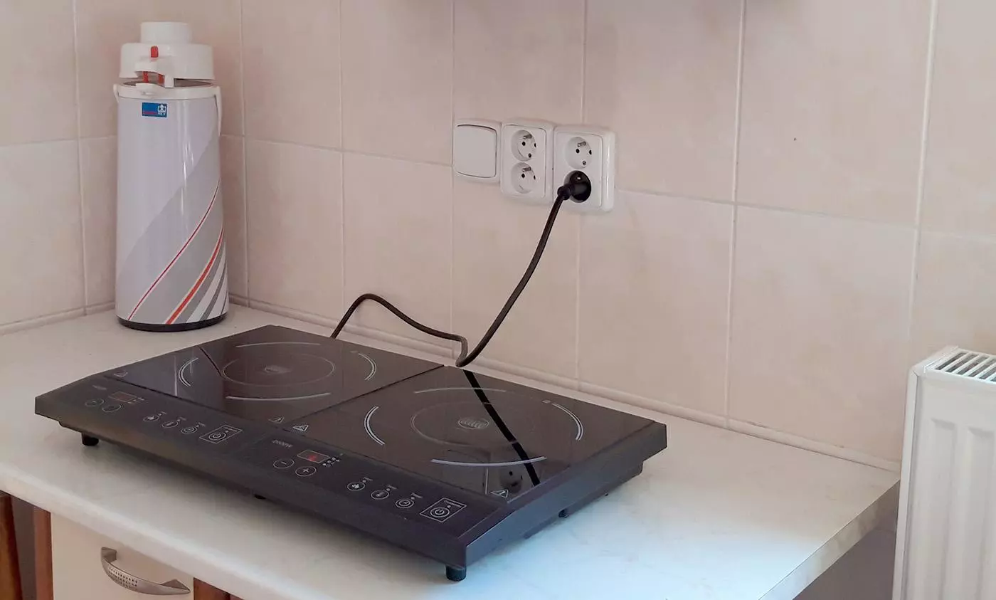 Indukční varná deska zapojená do elektrické zásuvky na kuchyňské zdi.