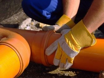 Ruce v žlutých rukavicích montují oranžové plastové kanalizační trubky.