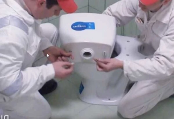 Dva pracovníci montují bílou toaletu na podlahu.