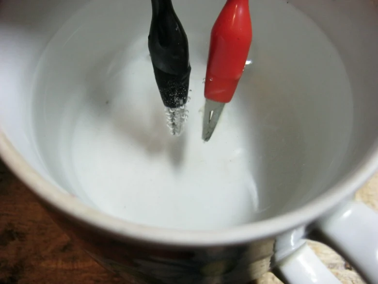 Červený a černý elektrický měřicí vodič ponořený ve vodě v šálku.