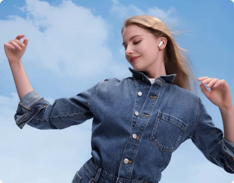 Žena s bezdrátovými sluchátky Huawei tančí pod modrou oblohou.