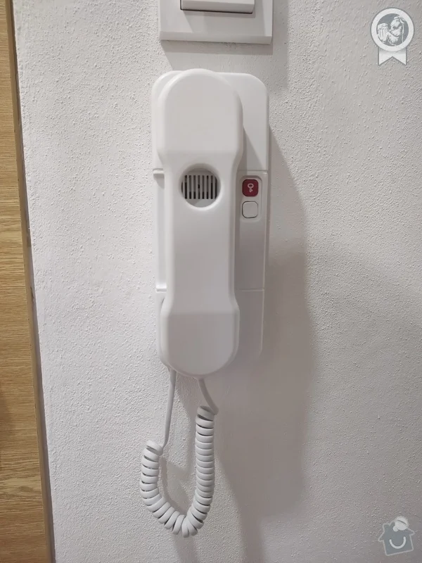 Bílý nástěnný telefon uvnitř domu na bílé zdi.