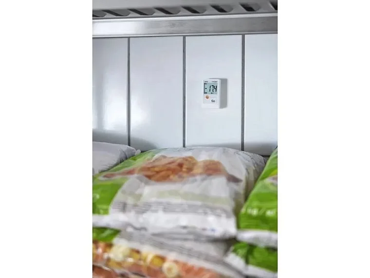 Digitální teploměr v mrazáku s balenými potravinami pro sledování teploty.