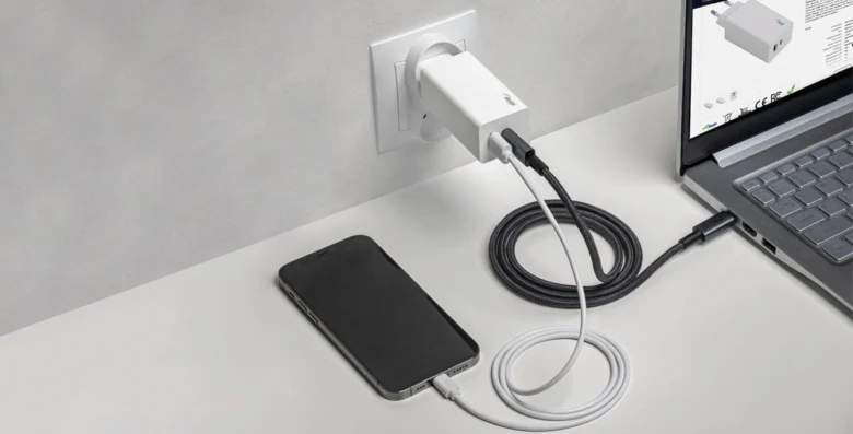 Bílý nabíječka s USB-C napájí notebook i telefon na čistém stole.