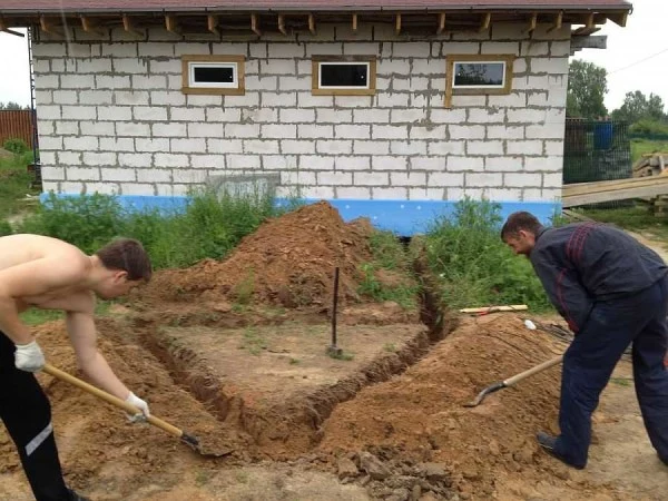 Dva muži ručně kopejí příkop pro uzemnění před domem.