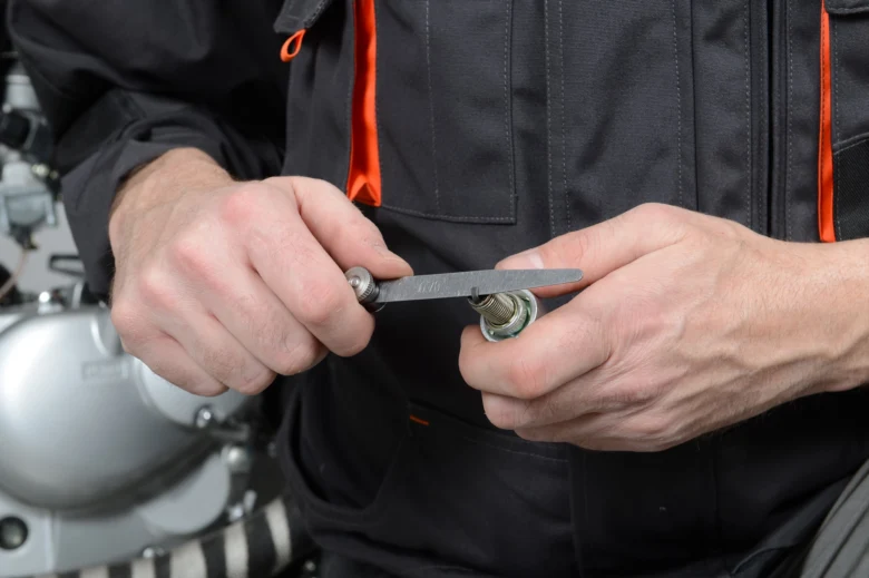 Mechanik nastavuje mezery mezi elektrodami zapalovací svíčky pomocí kalibru.