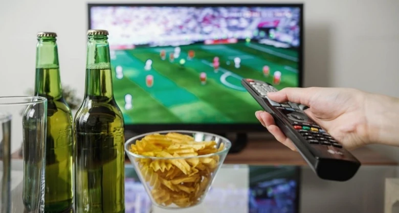 Ruka s dálkovým ovladačem před televizí hrající fotbal.