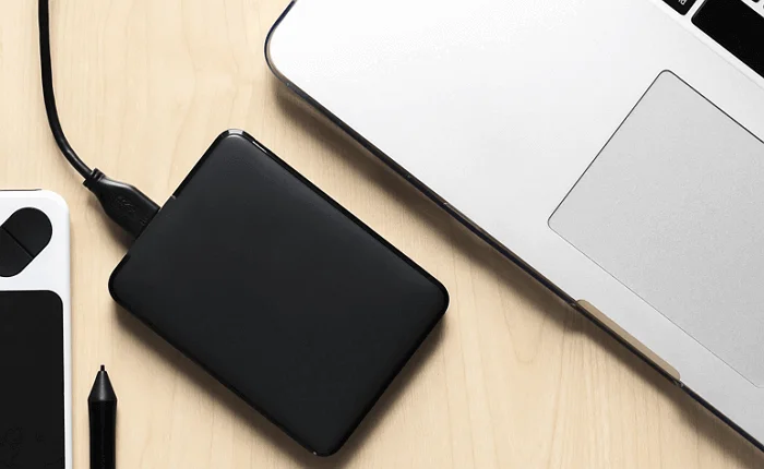 Externí pevný disk připojen k notebooku přes kabel USB na pracovní ploše.