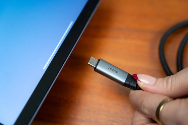 Ruka drží kabel s konektorem USB-C pro nabíjení notebooku.