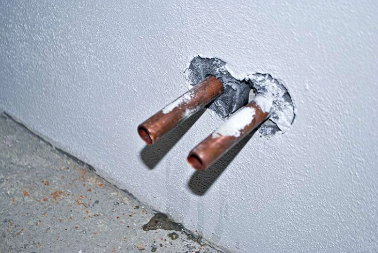 Dvě měděné trubky vyčnívající ze zdi pro připojení radiátoru.