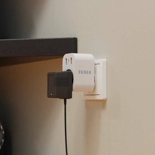 Bílá nabíječka Tesla zapojená do elektrické zásuvky na stěně.